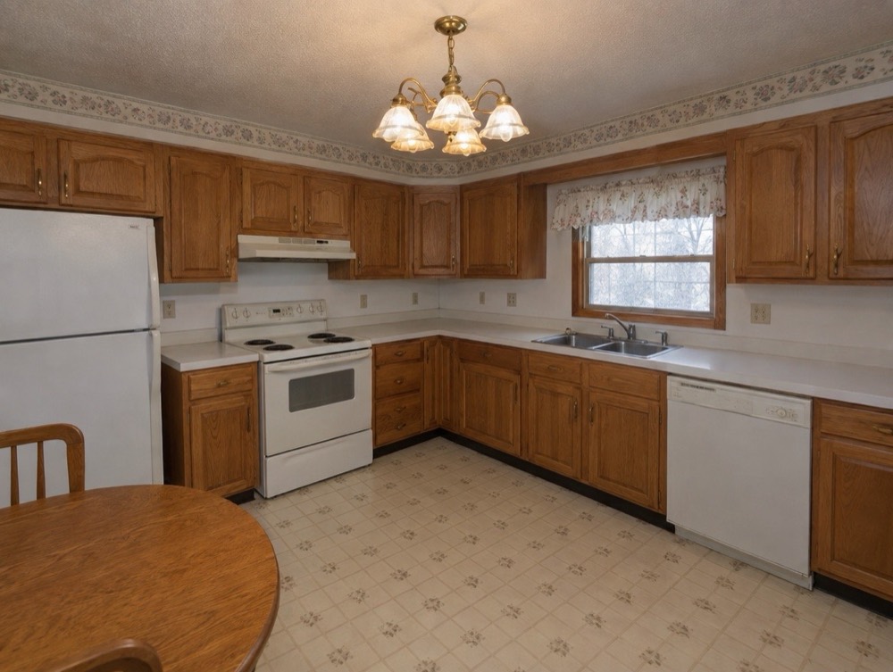 Before: Dated kitchen with honey oak cabinets, white appliances, laminate counters and a floral wallpaper border