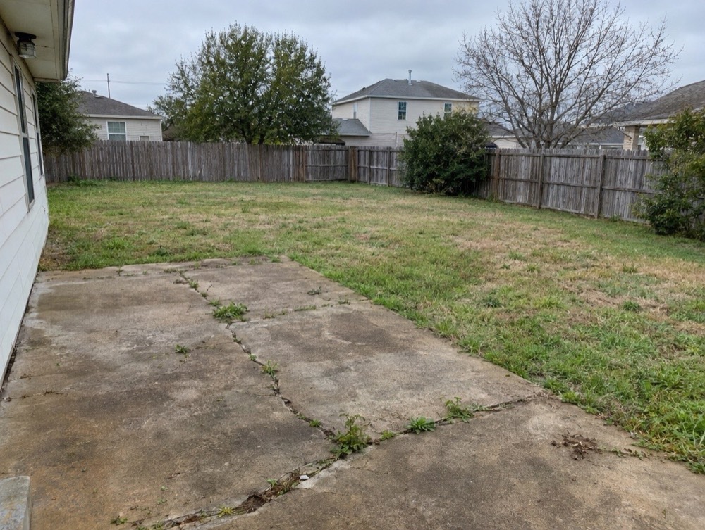 Before: Backyard with a cracked concrete slab, weeds in the seams and a patchy lawn